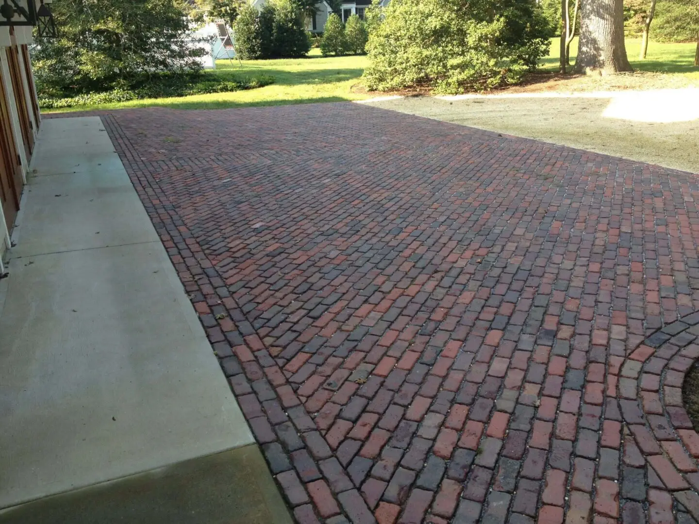 A clean brick driveway bordered by concrete edges in a sunny garden area.