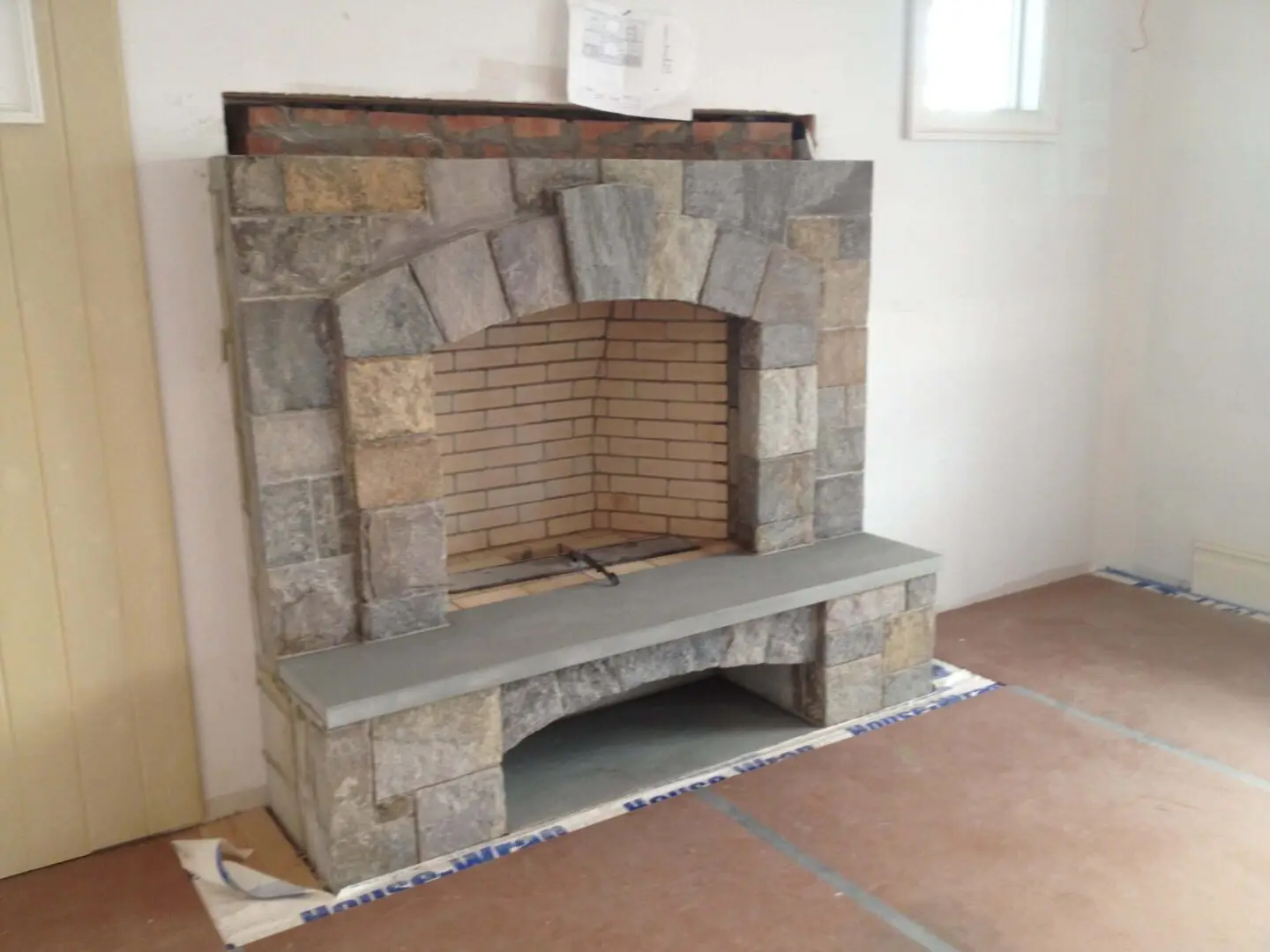 Stone fireplace with a curved opening and a bench in front.