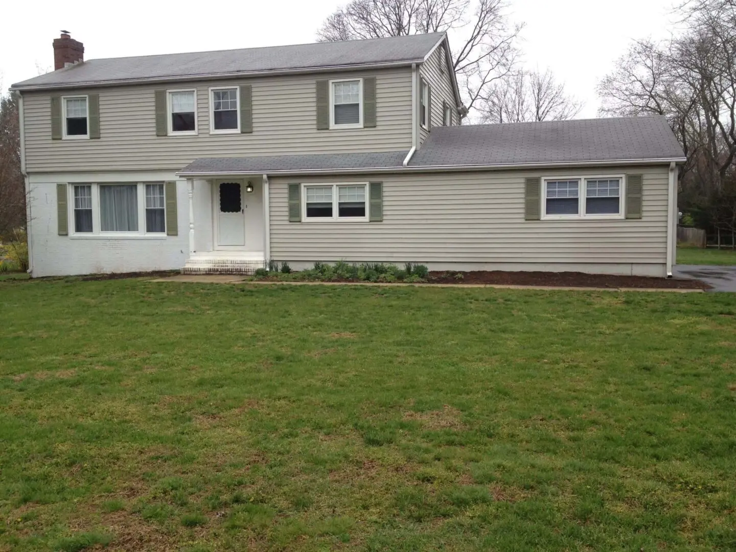 A beige two-story house with a large green lawn in front.