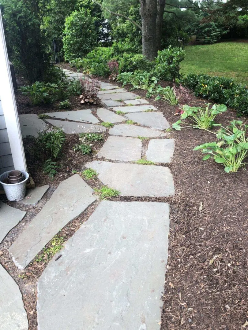 Stone pathway winding through a garden bed beside a house.