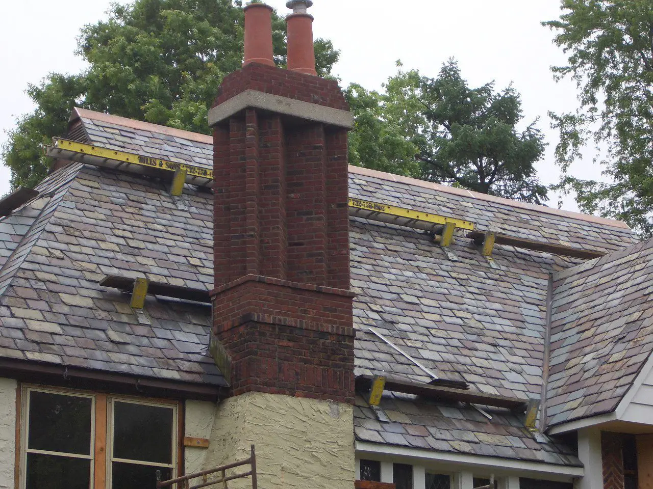 Tall brick chimney on a slate roof with moss patches.