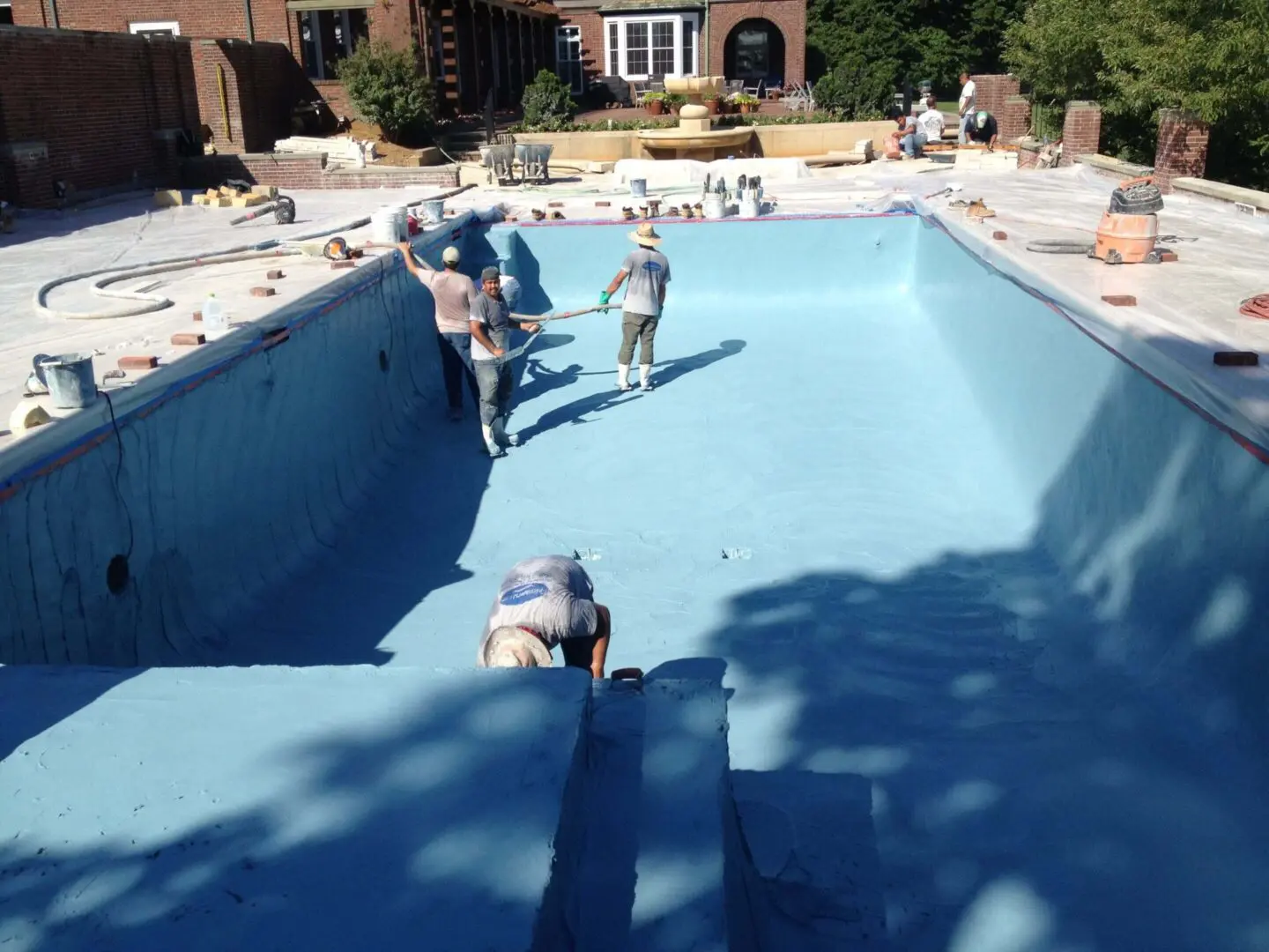 People cleaning an empty swimming pool on a sunny day.