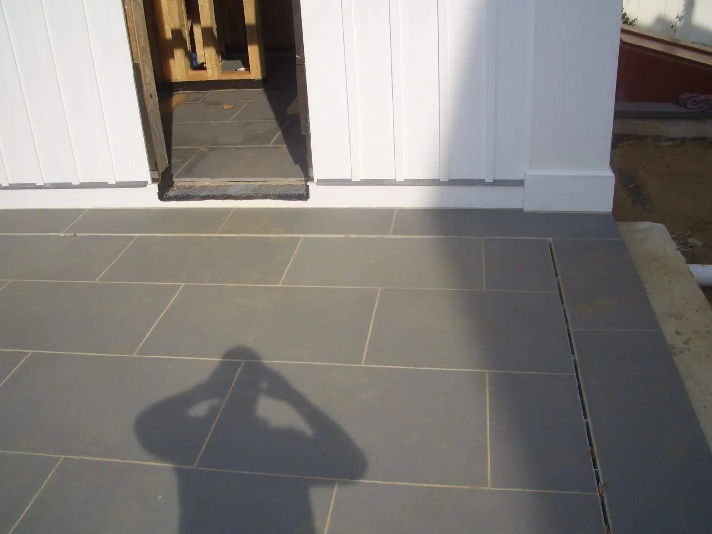Shadow of a person taking a photo on a tiled floor near a doorway.