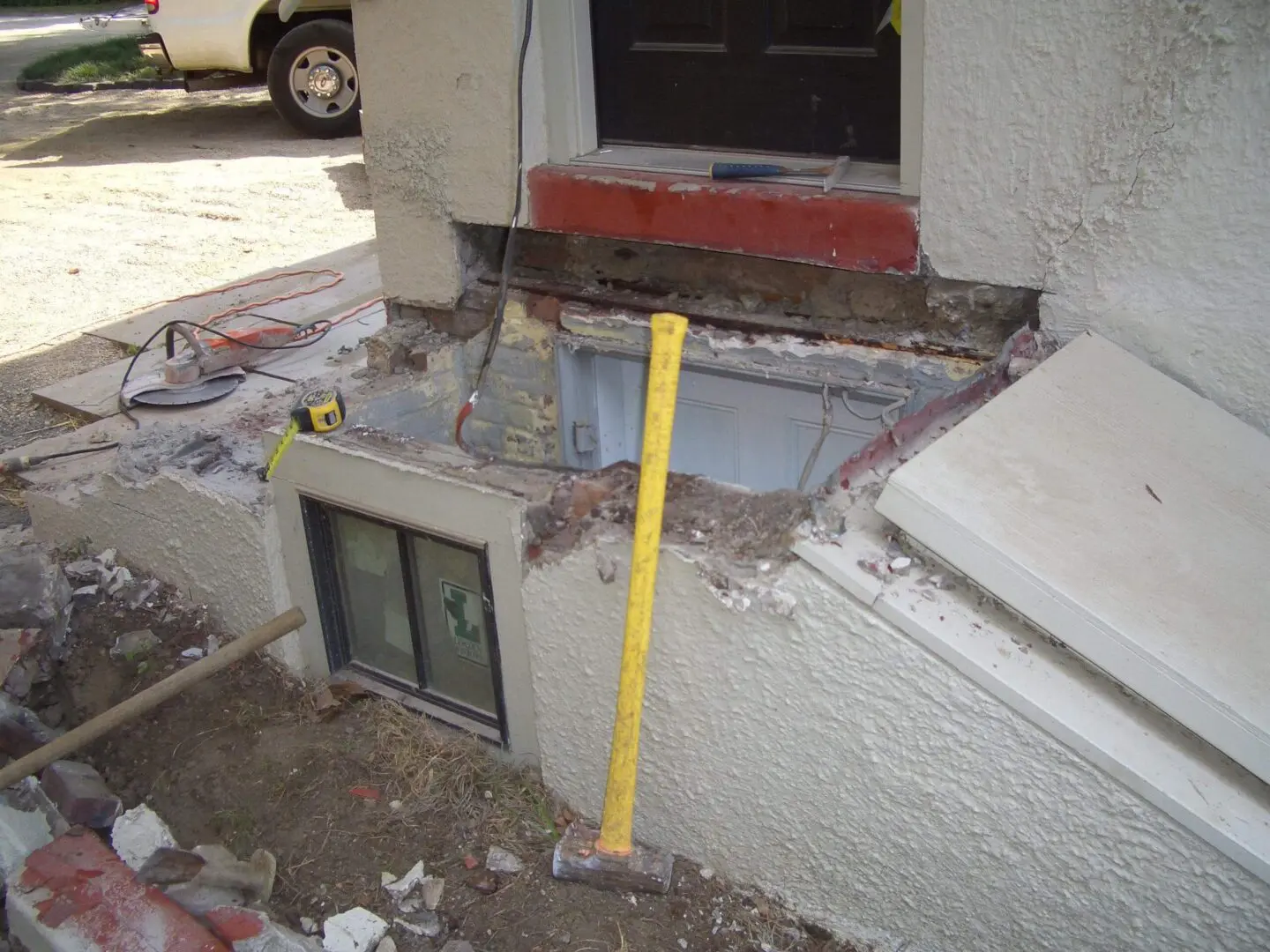 A small basement window partially covered by a concrete patch with a yellow tool nearby.
