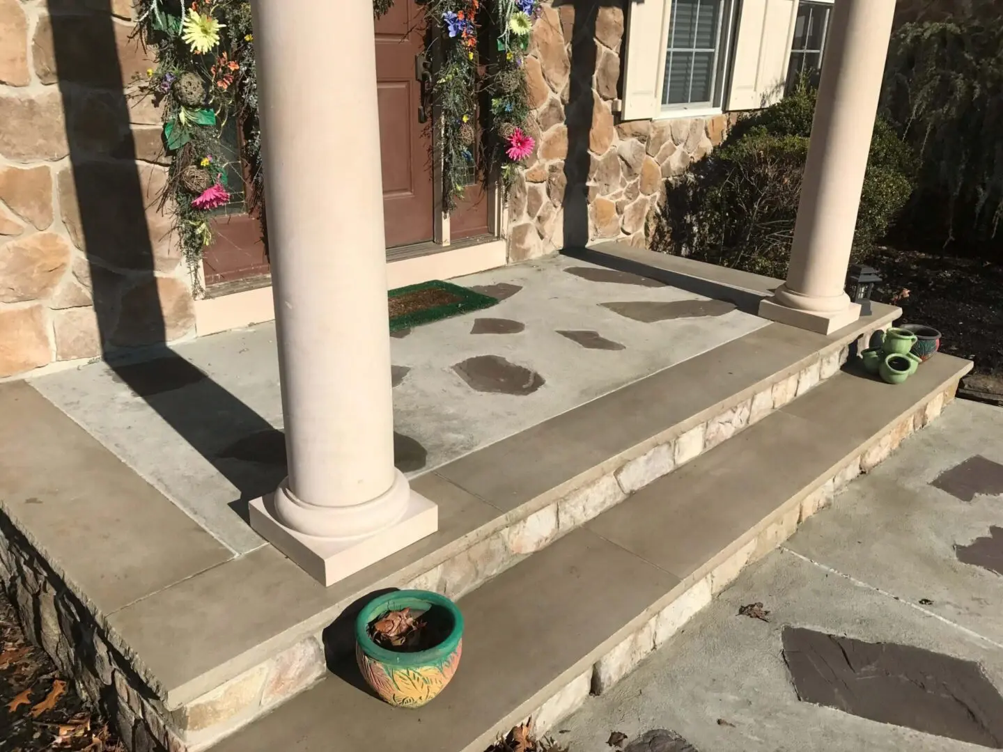 Front porch with stone steps, columns, and a small planter with flowers.