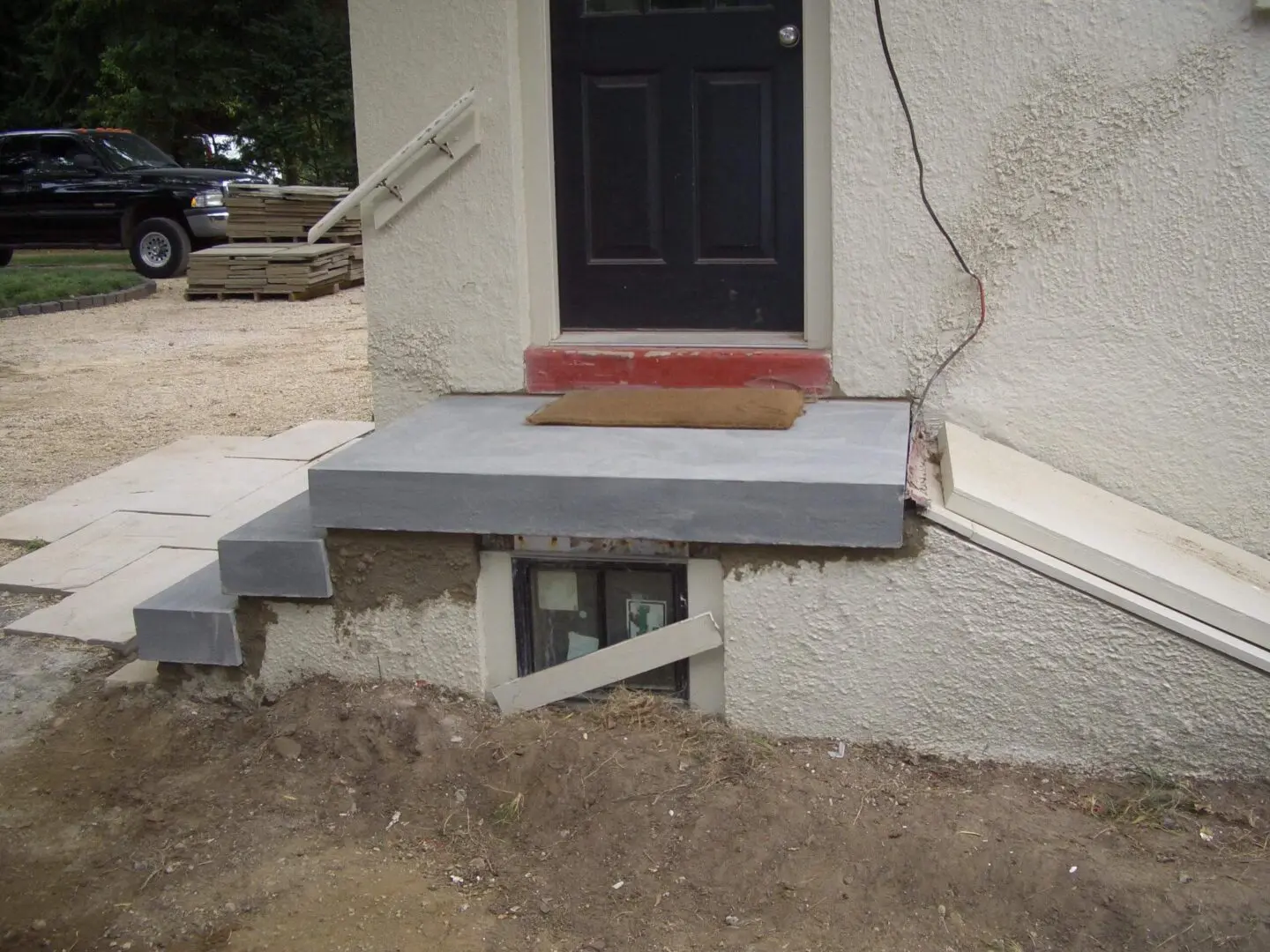 Small outdoor concrete steps leading to a black door above a basement window.