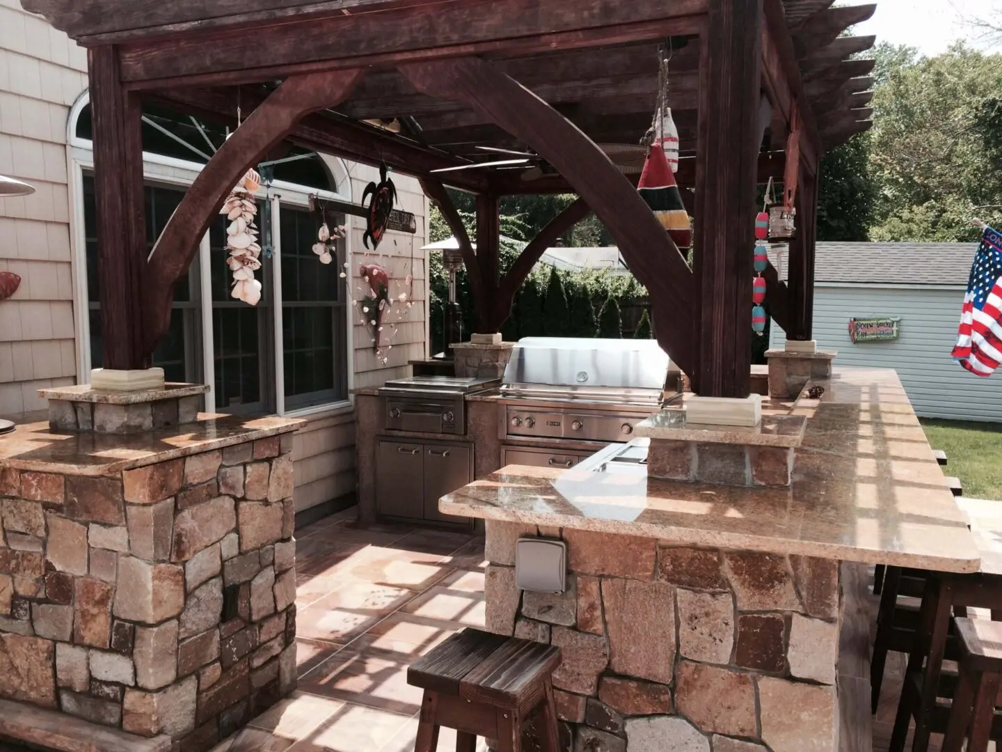 Outdoor kitchen with stone counters and wooden pergola.