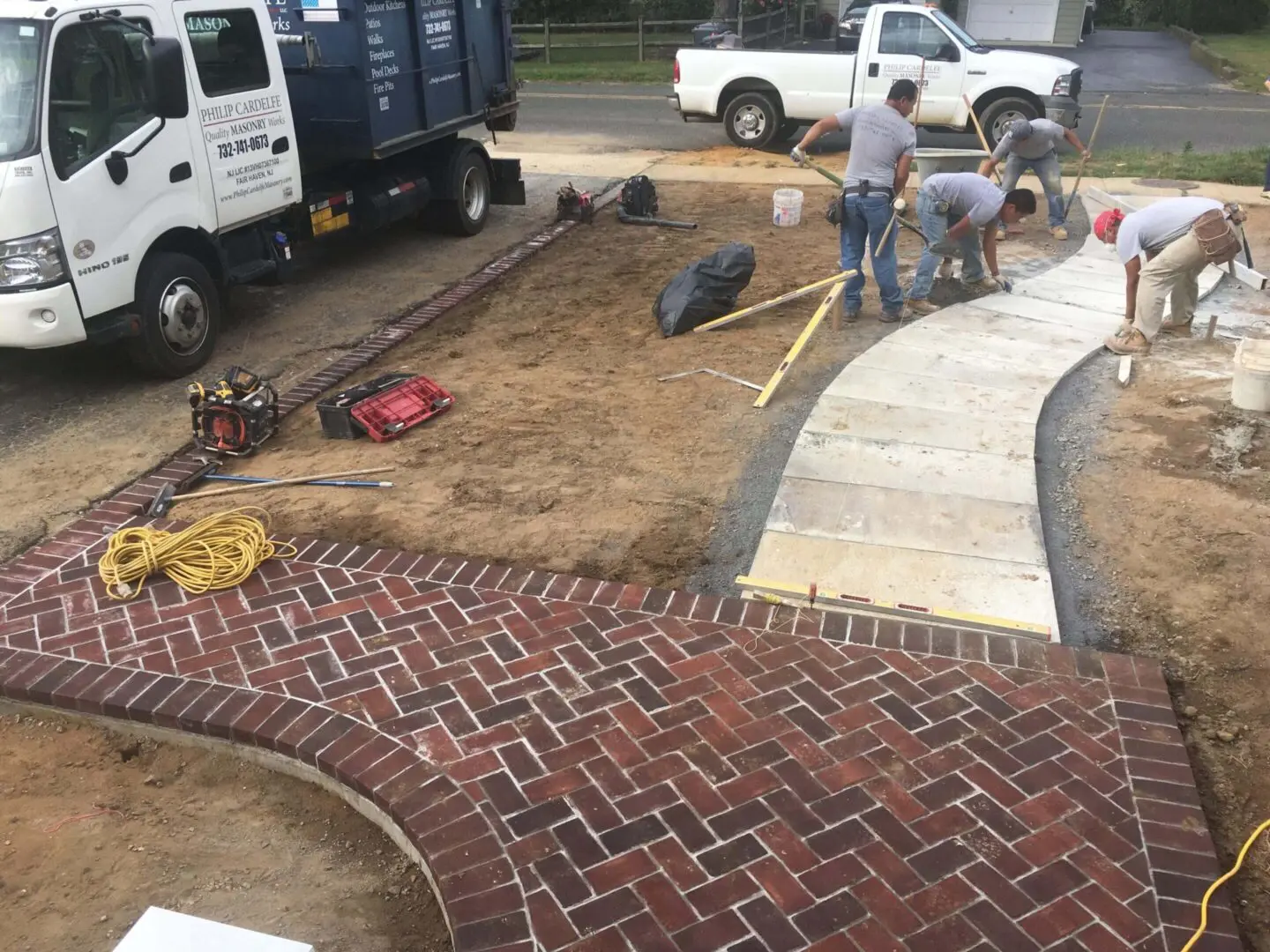 Workers constructing a brick pathway beside a curved concrete sidewalk.