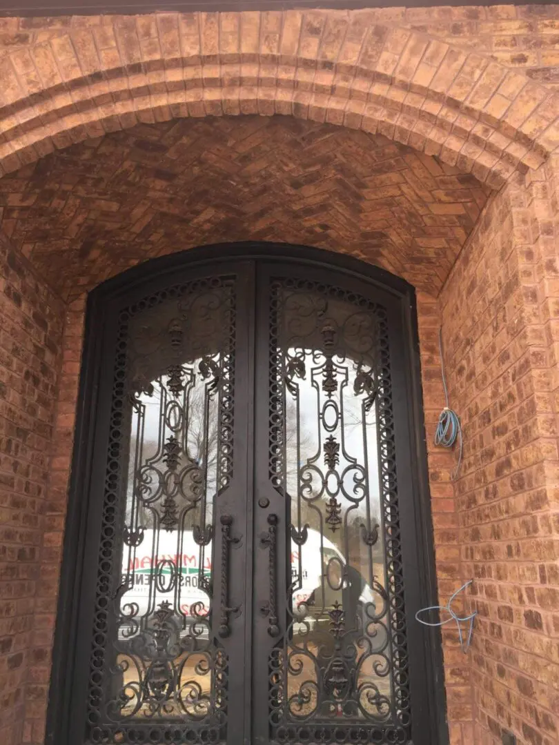 Elegant black wrought iron double doors with intricate designs set in a brick wall.